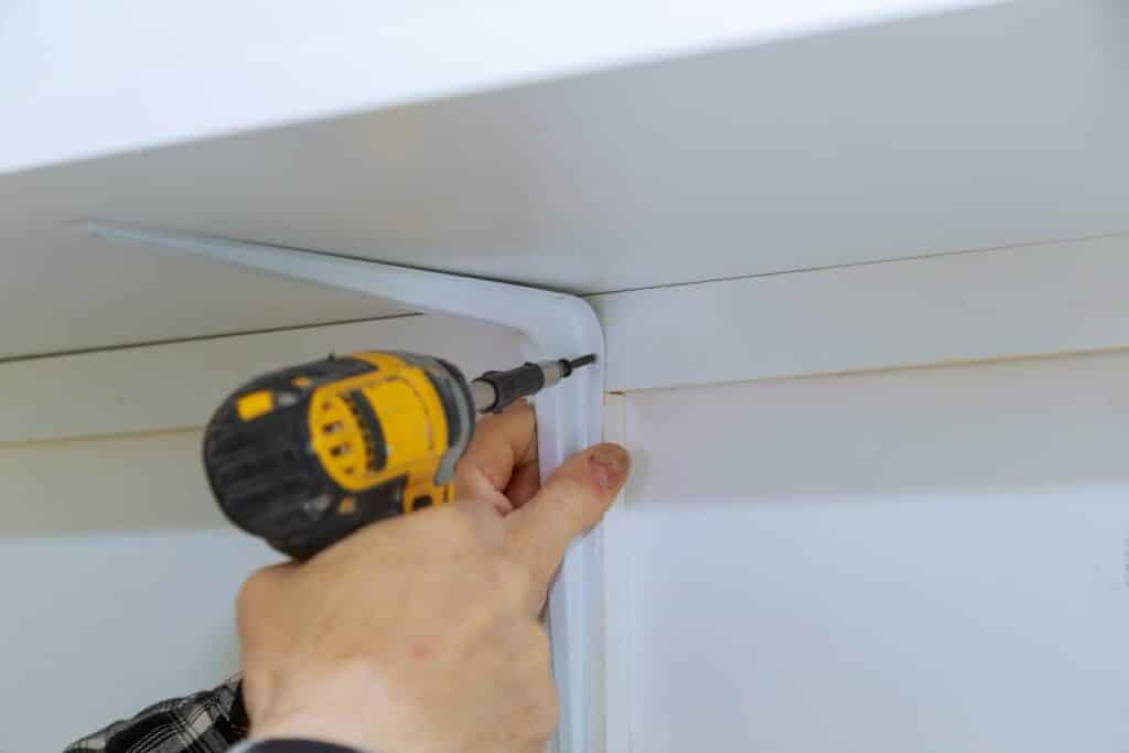 Man installing white shelving with a drill